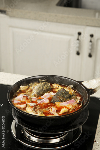 Spicy Poached Fish Fillets in Red Chili Oil Cooking in Black Pan on Kitchen Stove