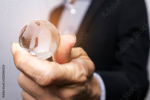 Businessman in suit holding a transparent globe, world investment and international business media