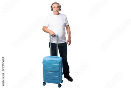 Konstfotografi Senior traveler wearing wireless headphones while standing with a rolling suitcase