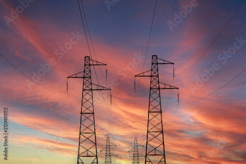 Silhouette of high voltage power pylons against a colorful sunset sky.