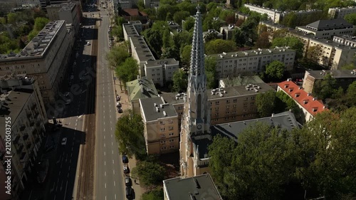 Aerial footage of a historic neo-Gothic church in Warsaw, surrounded by residential buildings, roads, trees and sunny Polish capital scenery.