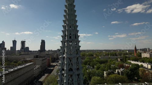 Aerial view of a neo-Gothic church tower in Warsaw, with detailed spire architecture, nearby streets, green trees and European city surroundings.
