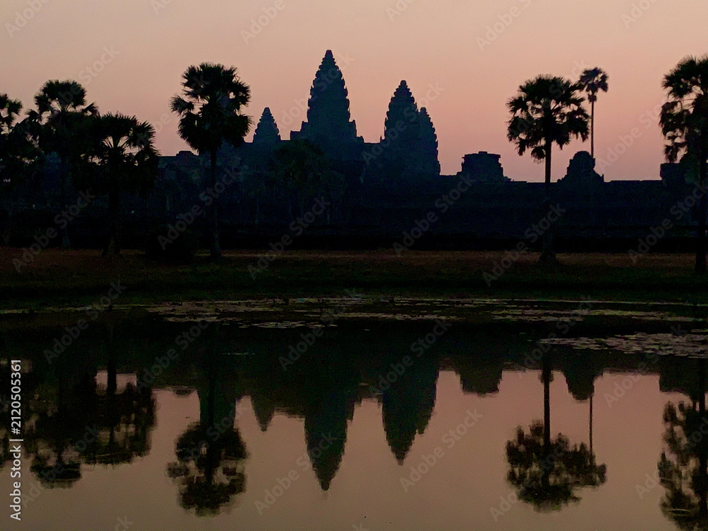 Fototapeta premium Siem Reap, Cambodia - February 20, 2020: Palm Trees and Angkor Wat Silhouetted at Twilight
