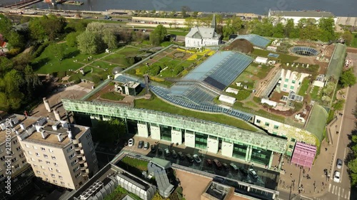 Drone footage over Warsaw rooftop garden with lush greenery, skylights, architectural lines and a calm urban landscape in sunny daytime weather.