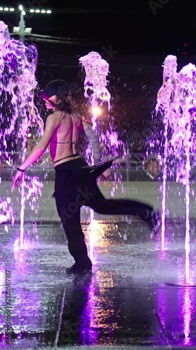 Stylish female dancing in fountain outdoor. Wet woman performing dance at night street. Youth subculture. Vertical video. Beautiful performance of girl in wet clothes. 4K, UHD