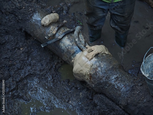 Close-up of an old cast-iron water pipe joint prepared for lead pouring, packed with oakum and sealed with a clay runner, with caulking tools on top.