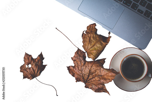 Laptop and coffee cup on a desk, surrounded by brown autumn leaves. Representing remote work, fall season, and comfort