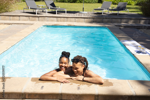 фотографія Couple leaning and smiling in backyard pool, wearing swimwear, towel with drinks