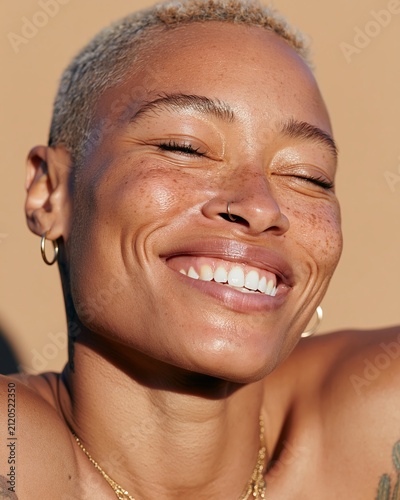 Diverse woman with short blonde hair and freckles smiling brightly against a neutral background, showcasing her joyful expression and natural beauty