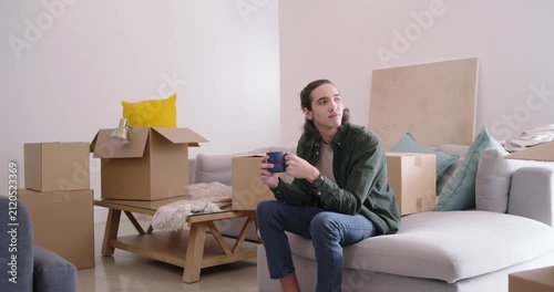 African American man sitting on light sectional sofa in apartment during move-in, sipping blue mug