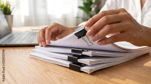 Detailed view of hands opening binder clipped file on wooden office tabletop.