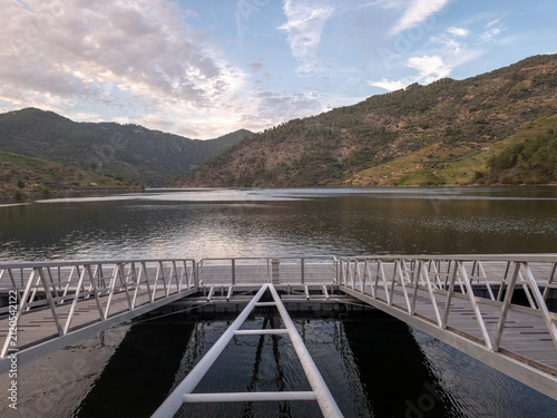 Peaceful view of the pier on the Tua River in São Mamede de Ribatua, Alijo, surrounded by rolling hills and the scenic Douro landscape at sunset.