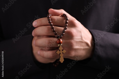 Photography Priest with rosary praying on black background, closeup