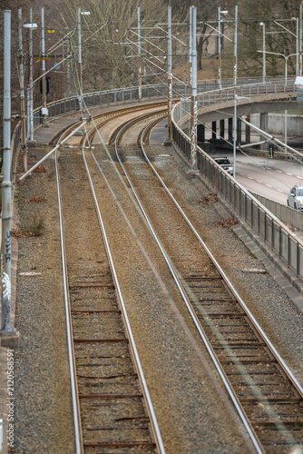 Railway tracks bending over elevated bridge beside roadway with urban infrastructure elements.