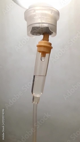 Close up of saline drip chamber with fluid drop in hospital room.