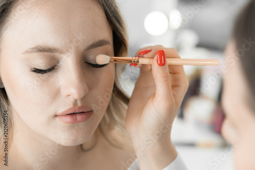 A skilled makeup artist carefully blends eyeshadow on a model's eyelid, focusing on precision and beauty trends. The scene captures modern cosmetics application in a bright, stylish environment
