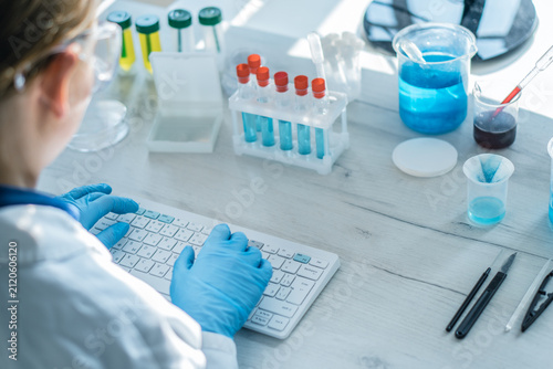 A laboratory professional analyzes scientific data on a computer surrounded by colorful chemical solutions and test tubes. Modern science, technology, and innovation in a clinical research environment