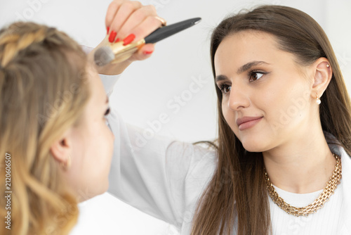 A skilled makeup artist uses a brush to enhance the complexion of a client during a makeup session. The scene captures a trendy beauty routine in a contemporary setting