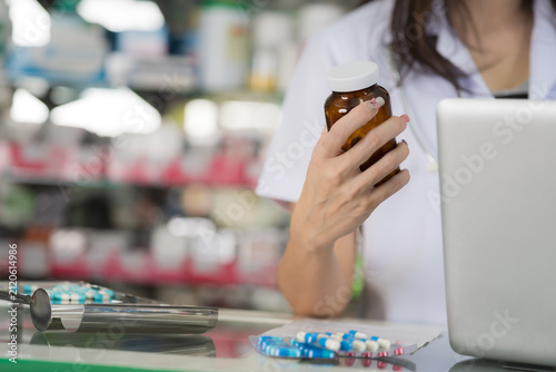 Pharmacist holding medication bottle near laptop and pills on counter