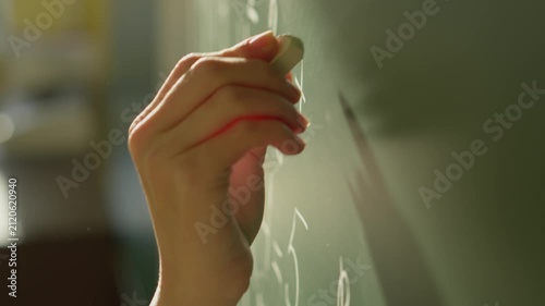 Person’s hand is captured in act writing with white chalk on traditional green chalkboard, symbolizing teaching, knowledge sharing. Evokes themes education, creativity, academic inspiration