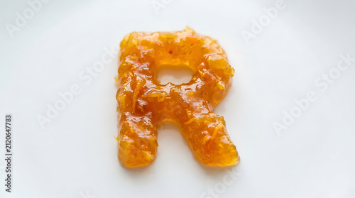 Orange marmalade is shaped into the letter R on a white plate.