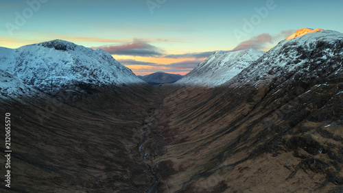 Scenic view of snow covered mountains in the Scottish Highlands at sunrise. Winter landscape with rugged peaks, natural textures and warm sunrise light. 