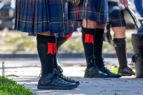 Canvastavla Scottish men, kilt wearers, standing on a sidewalk wearing Highland Games attire of traditional blue colored tartan kilts with knee-high black wool hose, flashes, leather sporrans, and black brogues