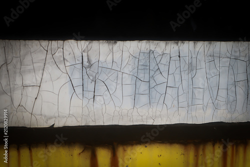 cracked white painted strip on dark rusty yellow metal surface, weathered old wall texture.