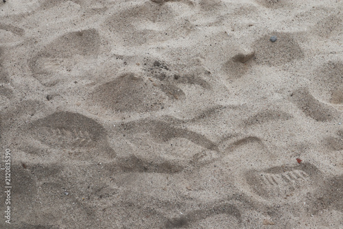 High angle view of shoe footprints stamped on fine beach sand surface, natural ground texture background.