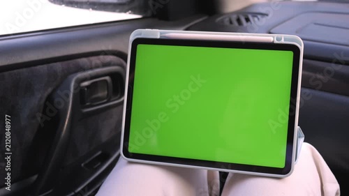 Hand interacts with a green screen tablet inside a car. The hand moves gently across the screen. The person appears calm and focused. Ideal for car tech or in-car entertainment content