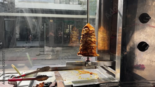 Shawarma Chicken Kebab on Vertical Rotisserie with Tools in Glass Case in street restaurant 