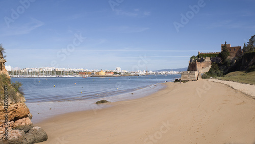 The historic Fort of São João do Arade stands beside the wide, sandy shores of Praia da Angrinha in Ferragudo, Algarve under a clear blue sky.