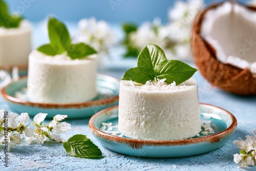 Coconut mousse cakes topped with fresh mint on blue plates with floral background in sharp focus for culinary branding