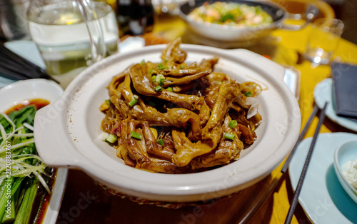 A delicious and savory dish of braised duck feet cooked in a clay pot with rich sauce and garnished with green onions, served in an Asian restaurant setting