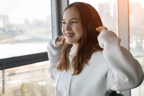 Foto Young woman smiling while listening to music through headphones, standing by a l