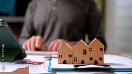 фотографія Small wooden house models rest atop financial paper documents businessman works background, calculating mortgage payment, real estate investment, property tax planning, home insurance cost
