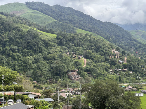 Принти на полотні A scenic view featuring a village, a river, lush green forests, mountains, the sky, and morning mist