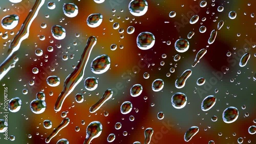 Beautiful water droplets and condensation on a window glass surface with a vibrant blurred autumn background of red and green colors