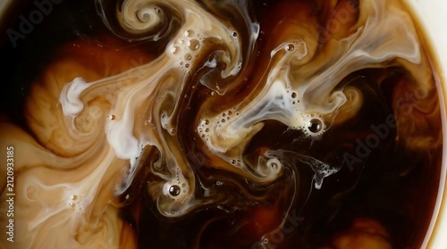 Macro swirl of milk mixing into dark coffee.
