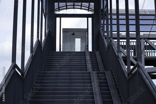 Wide steel staircase leading to a covered pedestrian overpass with bicycle ramps. Modern urban transportation infrastructure and accessibility.
