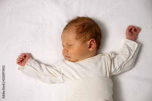 Tiny infant resting in deep slumber, showing innocence and tranquility against a simple white background, symbolizing new life and childhood