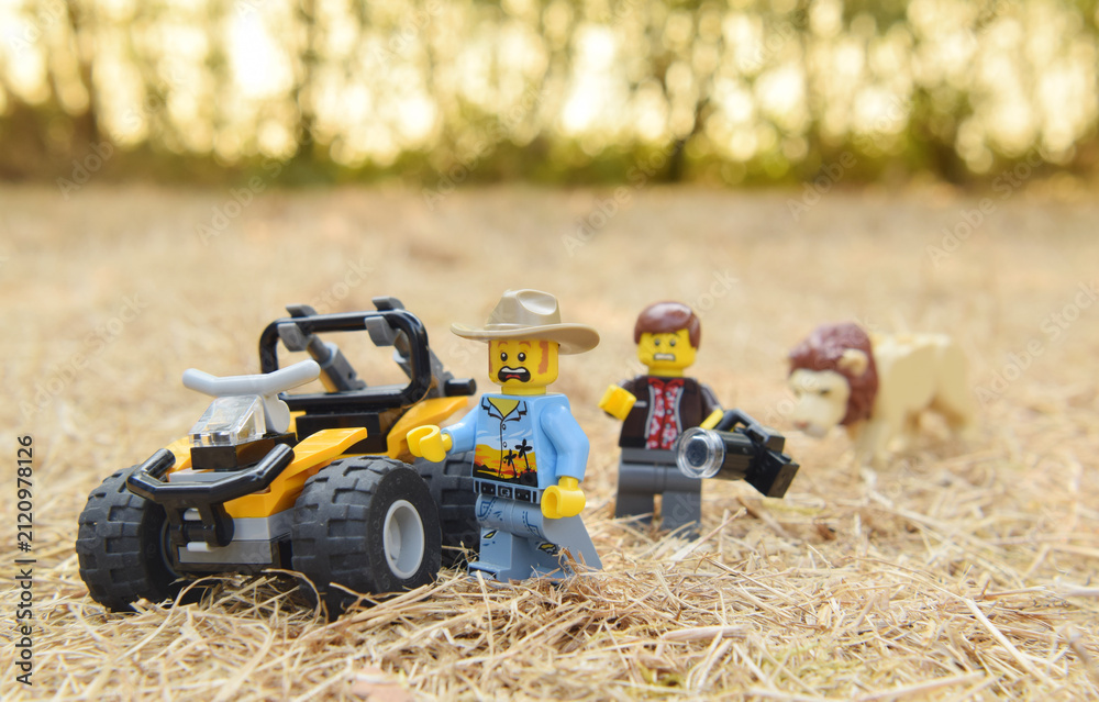 Fototapeta premium Lego minifigures of tourists are running away from the lion in the natural dried grass field. Editorial illustrative image of popular plastic toy.