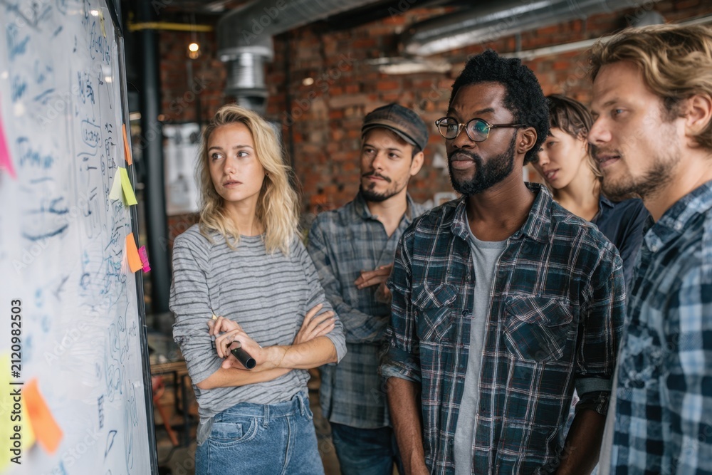 Obraz premium Multicultural team of five professionals engaged in discussion and brainstorming session at office space with ideas written on whiteboard