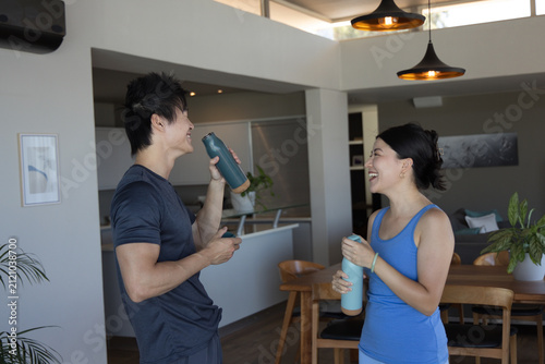 Obraz na plátně Asian couple in gym gear standing by kitchen island lifting water bottles, laugh