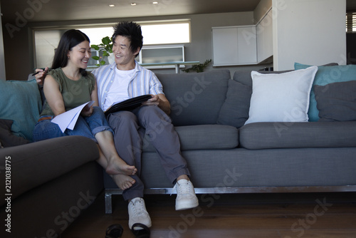 Obraz na plátně Diverse couple sitting on gray sectional sofa at home, reviewing papers and tabl