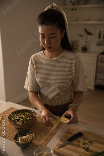 фотографія African adult woman wearing striped top halving hardboiled egg on cutting board
