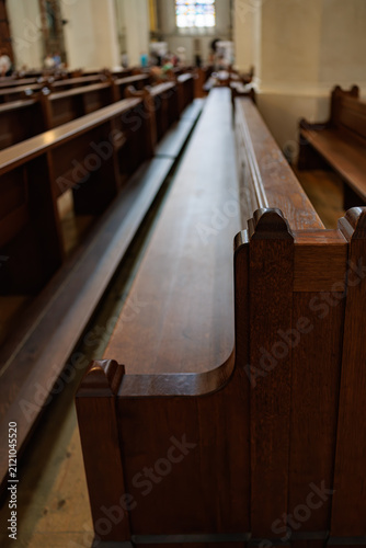 Принти на полотні Rows of polished dark oak pews receding into a Gothic church interior, with a carved pew end in sharp focus in the foreground