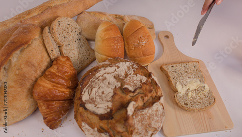 Bild auf Leinwand Spreading Creamy Butter on Multigrain Bread Slice with Bakery Assortment