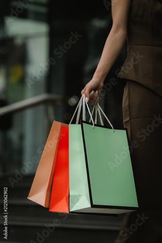 Close-up of a woman carrying colorful shopping bags outside a modern shopping mall, representing retail, consumer lifestyle, fashion, and successful shopping.