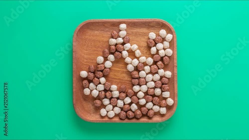 Stopmotion: eating chocolate corn balls from a wooden square plate. Top view, close-up, green background	